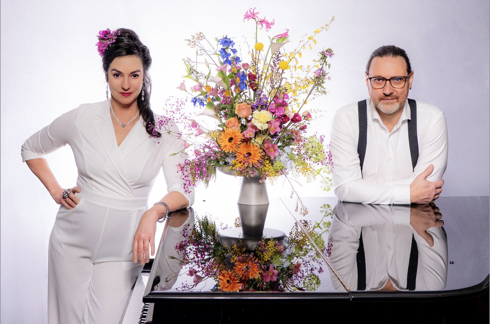 Franziska in weißem Anzug und Markus stehen am schwarzen Flügel, zwischen beiden ein prächtig bunter Blumenstrauß