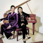 Franziska Dannheim und Jeong-Min Kim sitzen gemeinsam auf der Bank vor einem braunen Flügel, heller Hintergrund