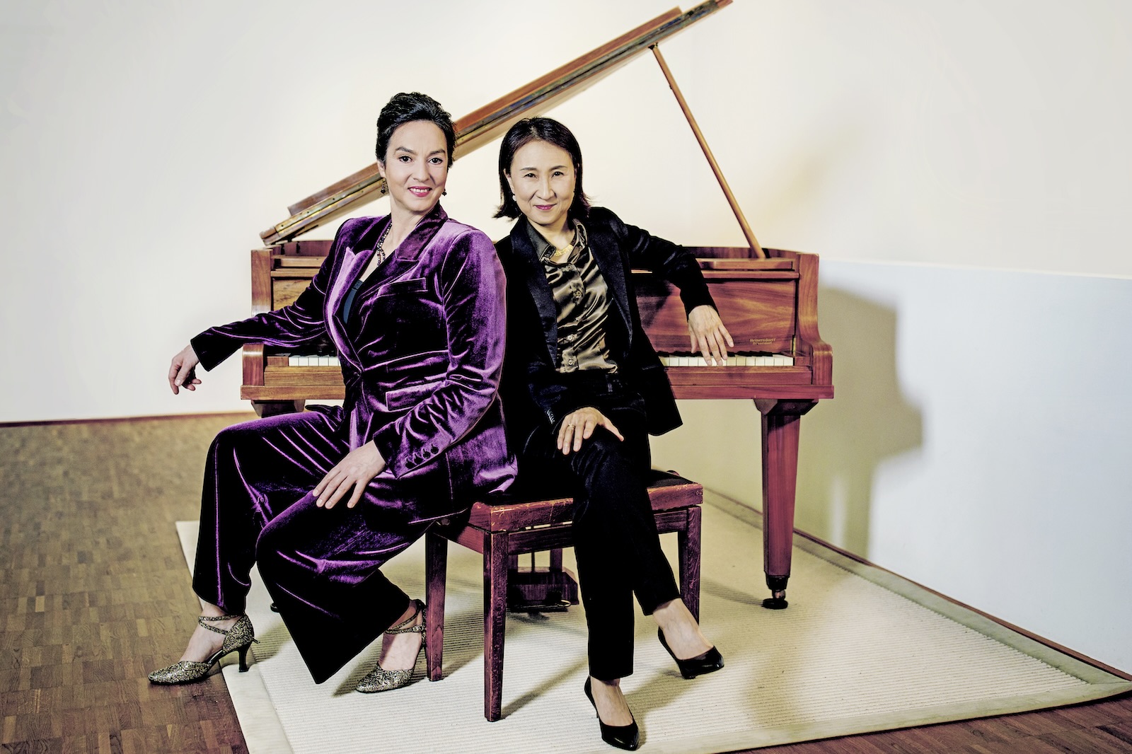 Franziska Dannheim und Jeong-Min Kim sitzen gemeinsam auf der Bank vor einem braunen Flügel, heller Hintergrund