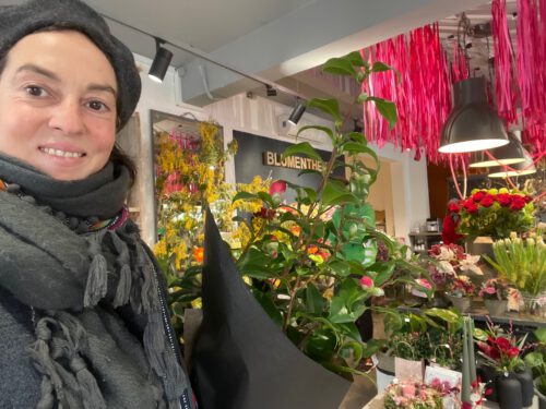 Frau steht im Blumenladen, bunte Blumenvielfalt im Hintergrund