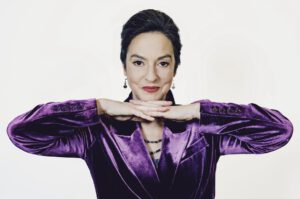 Franziska im lila Samt-Anzug vor weißem Hintergrund, Blick in die Kamera